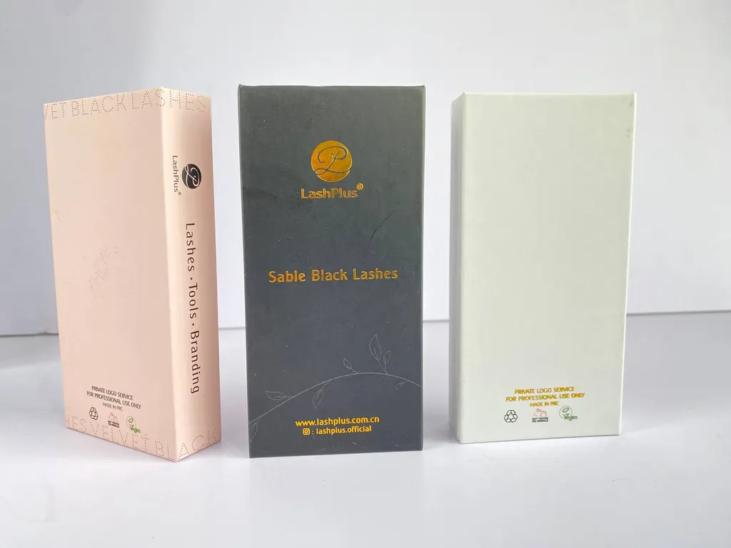 Three closed premium lash boxes standing together: matte pink, black with a gold logo, and cream